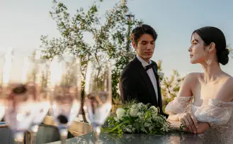 新郎新婦が、パティオで結婚式を挙げている最中、シャンパングラスの近くに立っています。屋外での温かな雰囲気の中で、二人は厳粛でロマンチックな瞬間を共有しています。